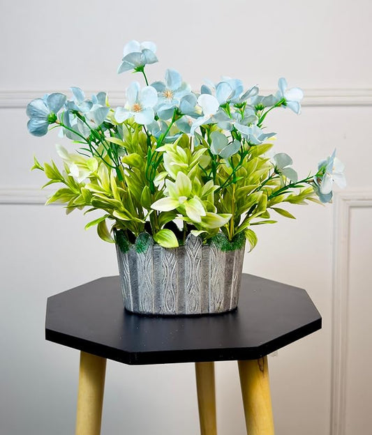 Artificial plant in a decorative pot on a hexagonal black table with yellow legs against a light-colored wall.