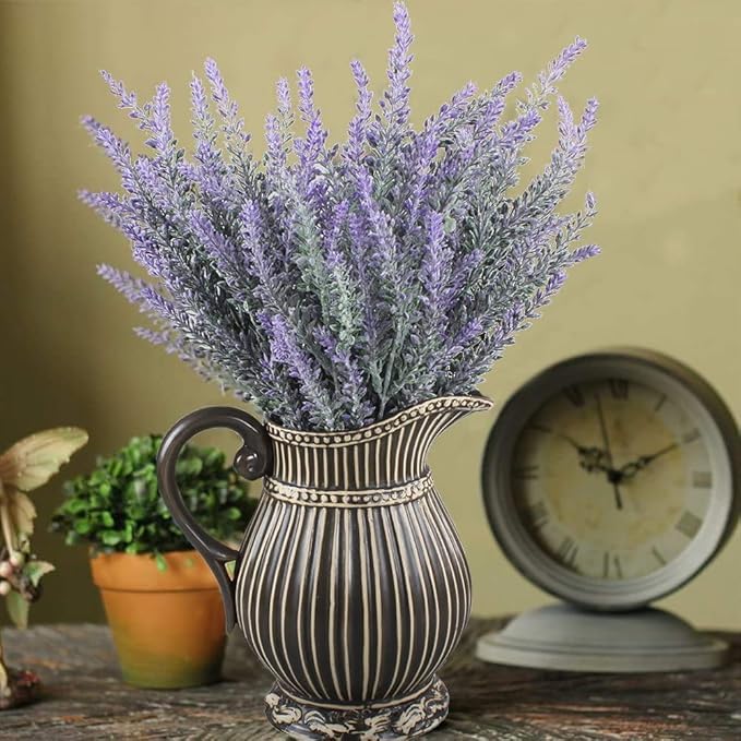 Decorative vase with lavender flowers on a table with a clock and plant in the background.