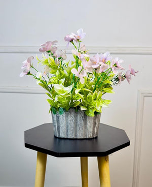 Artificial flower arrangement in a decorative pot on a hexagonal table against a white wall.