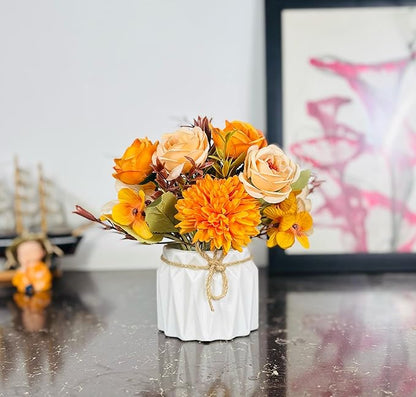 White ceramic vase with a bouquet of orange and yellow flowers on a reflective surface.