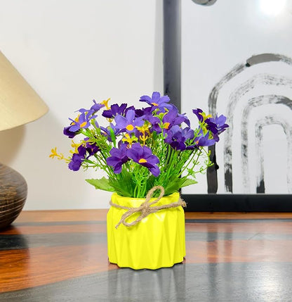 Yellow vase with purple and green flowers on a wooden surface