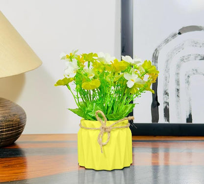 Yellow vase with greenery on a wooden surface next to a lamp and framed picture.