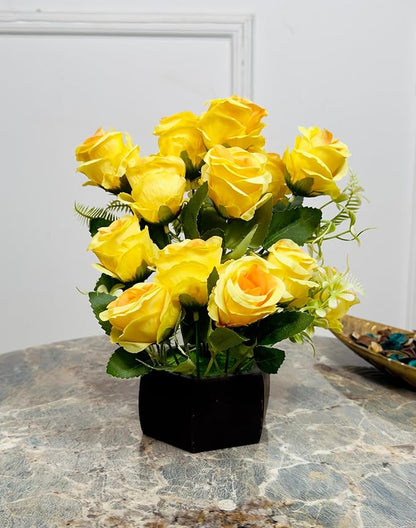 Bouquet of yellow roses in a black vase on a marble surface with a white wall background.