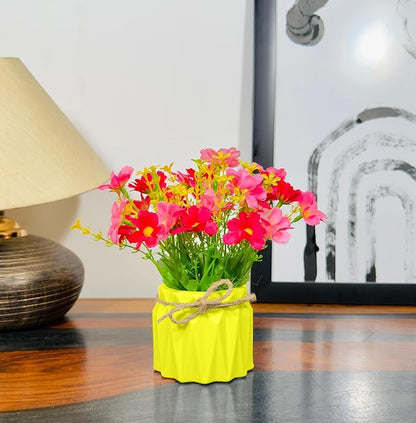 Yellow vase with colorful flowers on a wooden surface next to a lamp and framed picture.