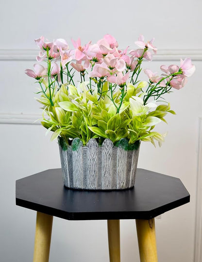 Potted plant with pink and green flowers on a hexagonal black table against a light gray wall.