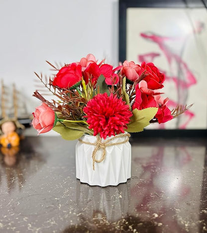 Small white vase with red and pink flowers on a reflective surface