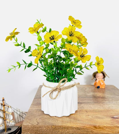 Yellow flowers in a white vase on a wooden surface with a small figurine in the background.