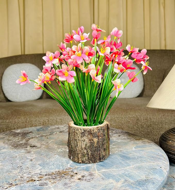 Bouquet of pink flowers in a wooden vase on a marble table with a beige sofa in the background.